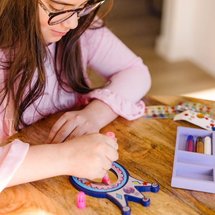 A kid playing with the Melissa & Doug Decorate-Your-Own Wooden Princess Mirror Craft Kit