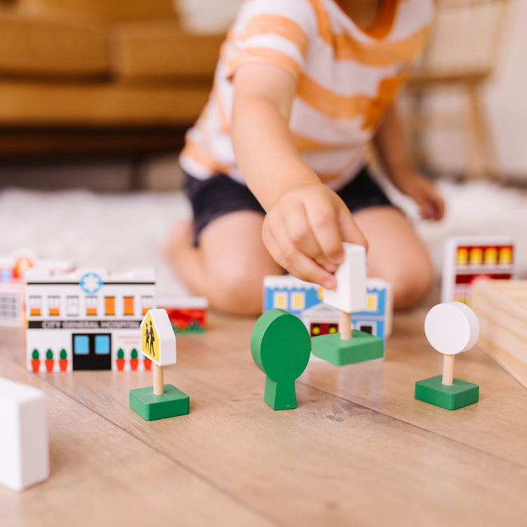 A kid playing with the Melissa & Doug Wooden Town Play Set With Storage Tray (32 pcs)